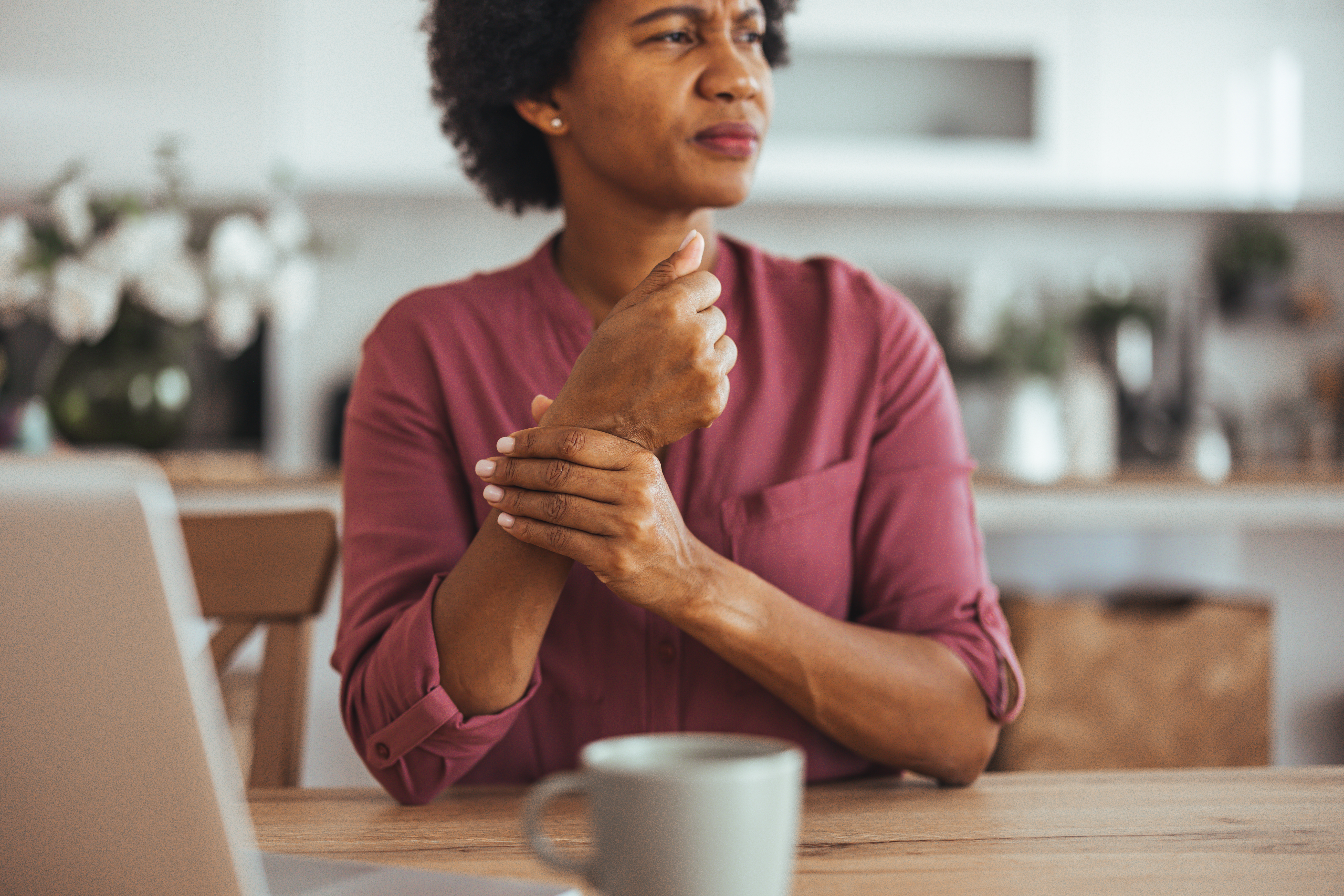 Woman sitting in a kitchen holding her wrist which sufferes from arthritis